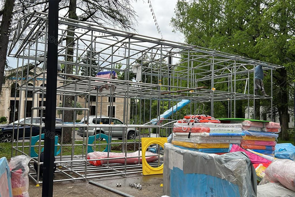 On-site installation progress of the Hooplo playground in Tskaltubo, Georgia: metal frame being assembled with play components ready for setup